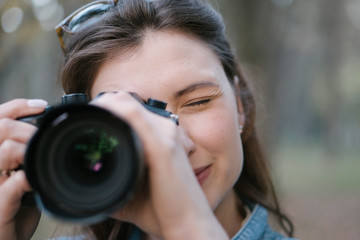 A girl with brown hair takes a picture on a mirrorless camera. A portrait of a photographer with a camera in her hands close-up