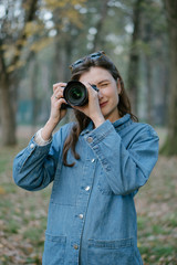 Portrait of a professional freelancer with a camera in hand in the autumn forest at sunset. The girl smiles and looks into the camera