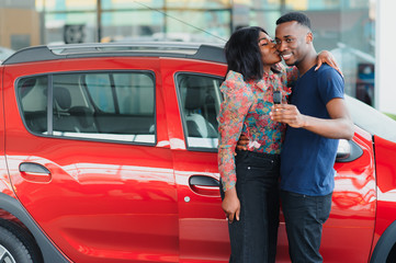 Smiling African American couple hugging and smiling at camera at new car showroom