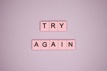 Try again word wooden cubes on pink background. Motivational poster.