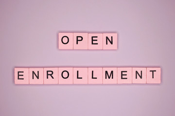 Open enrollment word wooden cubes on pink background.