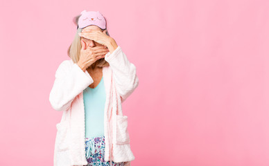 middle age woman covering face with both hands saying no to the camera! refusing pictures or...