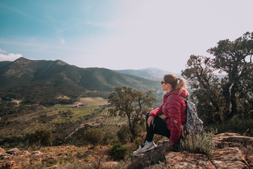 Young woman enjoying view on mountains in sunset, beautiful nature scenery with mountain tops. Girl or woman traveler with backpack alone, woman travelling solo, view from behind, vacation concept