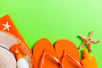 Summer beach flat lay accessories. Sunscreen bottle cream, straw hat, flip flops, towel and seashells on colored Background. Travel holiday concept with copy space