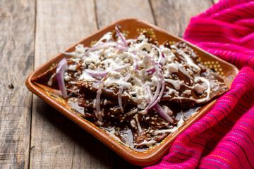 Mexican chilaquiles with mole sauce and fresh cheese on wooden background