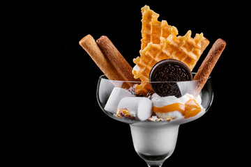 tasty vanilla ice cream poured with salt caramel with marshmallows waffles and chocolate chip cookies on a black background isolated