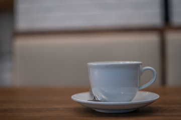 	
The white ceramic coffee cup with coaster is placed on a brown wooden base on the back, naturally a blurred background.