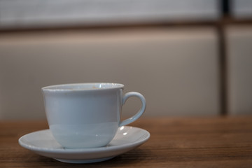 	
The white ceramic coffee cup with coaster is placed on a brown wooden base on the back, naturally a blurred background.