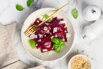 Homemade beetroot ravioli with goat cheese, pine nuts and basil in a plate on a marble background. Healthy food. Beet ravioli stuffed with baked beets. Top view