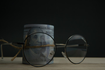 Fototapeta na wymiar Eye glasses and roll of money dollar tied up on black background. Quotes and finance concept.