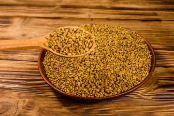 Ceramic plate and spoon with fenugreek seeds on wooden table