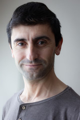 Fototapeta premium Headshot of smiling dark hair man. Happy portrait of young male model with brown cotton shirt. Soft natural light on right side of face. Photography lighting concept