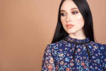 Portrait of a model, a beautiful brunette girl on a beige background, in a blue dress with blue eyes. The concept of female beauty.