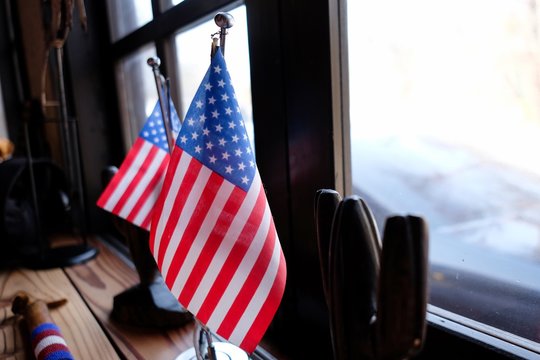 Closeup shot of two small U.S. flags placed on a table beside a window