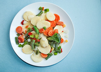 Frozen vegetables, close-up. Mix of vegetables on a white plate. Blue background.
