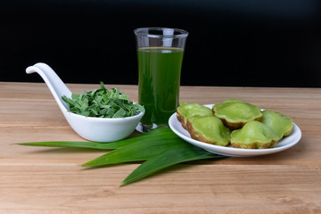 Siam Pandan Thai dessert with plate, water and pandan leaves on a dark wooden floor.