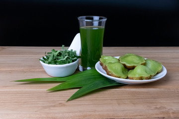 Siam Pandan Thai dessert with plate, water and pandan leaves on a dark wooden floor.