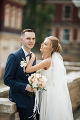 Wedding photo shooting. Bride and bridegroom walking in the city. Married couple embracing and looking at each other. Holding bouquet. Outdoor, full body