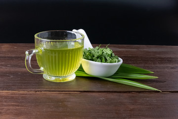 Pandan juice and leaves in a cup on a wood top, dark background.