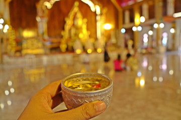 Hand holding bowl of scented water to sprinkle water onto a Buddha image, a gesture of worship during the annual Songkran festival. Religion and holiday concept.