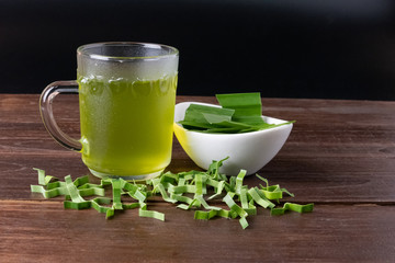 Pandan juice and leaves in a glass on a wood top, dark background.