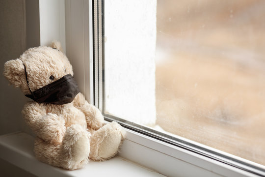 Teddy bear in a black mask is sitting by the window closeup