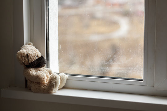Teddy bear in a black mask is sitting by the window