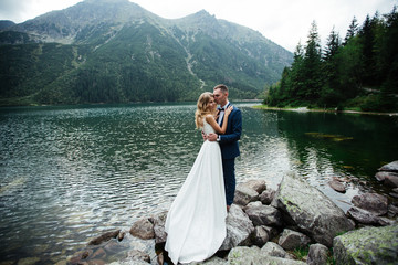 Beautiful wedding photo on mountain lake. Happy Asian couple in love, bride in white dress and groom in suit are photographed against background of the Kazakh landscape