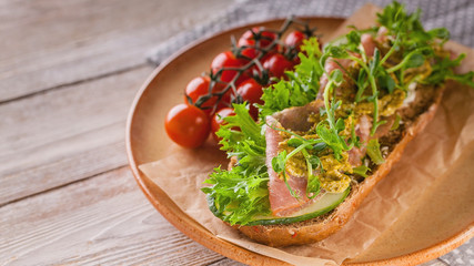 Close up bruschetta with raw smoked meat, cream cheese, pea microgreens and pesto sauce, cherry tomatoes on a wooden table