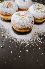 Donuts in powdered sugar and colored sprinkles on a black background. 