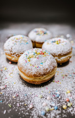Donuts in powdered sugar and colored sprinkles on a black background. 