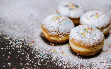 Donuts in powdered sugar and colored sprinkles on a black background. 