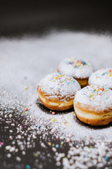 Donuts in powdered sugar and colored sprinkles on a black background. 