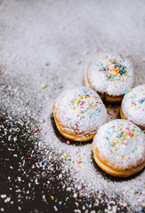 Donuts in powdered sugar and colored sprinkles on a black background. 