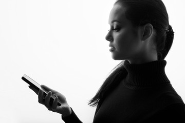 Beautiful young woman in a black dress with phone in her hand. Girl browsing internet on smartphone. White background. Free space for text.