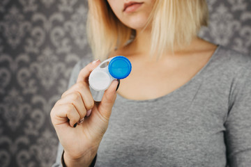 Naklejka premium blonde girl holds case for storing contact lenses for eyes, close-up cut photo