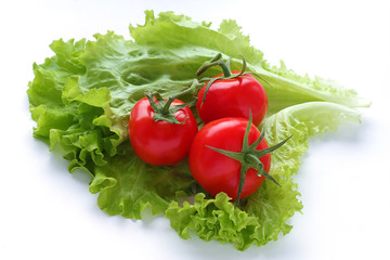 Red fresh tomatoes three pieces and green lettuce leaves lie on a white plain background. Vegetarian diet. Selective focus.