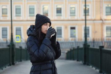 A girl with a glass of coffee on the street. Warmly dressed and smiling