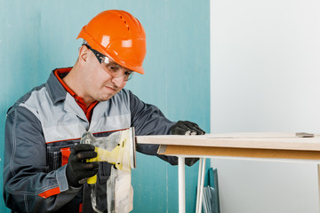 A young man, a carpenter polishes a wooden Board with an orbital sander. The concept of...
