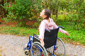Fototapeta na wymiar Young happy handicap woman in wheelchair on road in hospital park enjoying freedom. Paralyzed girl in invalid chair for disabled people outdoor in nature. Rehabilitation concept.