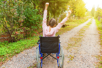 Young happy handicap woman in wheelchair on road in hospital park enjoying freedom. Paralyzed girl...