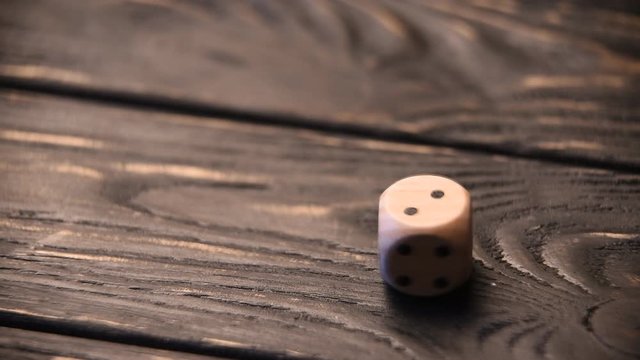 Wooden dice rolls on wooden table. Rolling all outcomes from one to six on the top side.