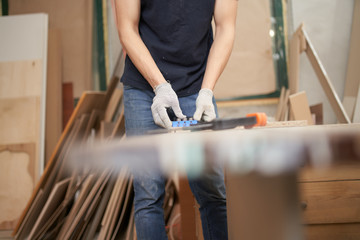Carpenter in white gloves with drill and board in workshop