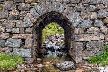Mountain stream leading under stone bridge arch in Scottish Highlands
