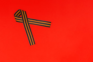 Ribbon of St. George on a red background for Victory Day. May 9, 2020 - 75 years of Victory in the Great Patriotic War. Flat lay, copy space, top view.