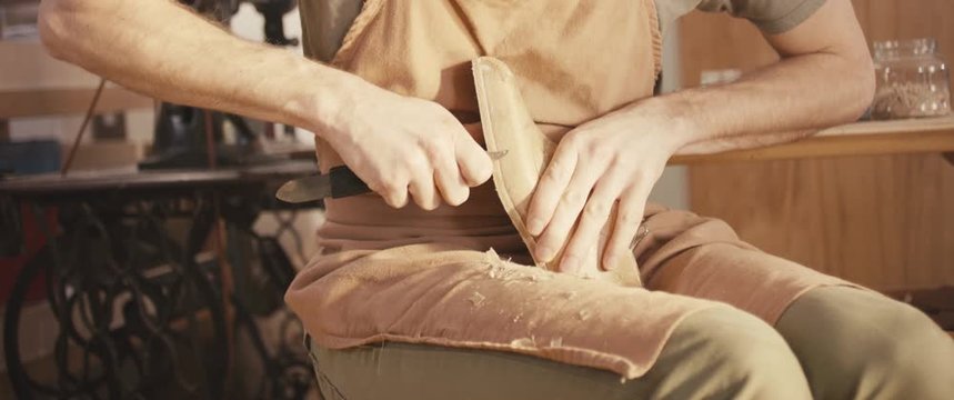 Traditional bespoke shoemaker cutting shaping leather insole on wooden shoe last with knife