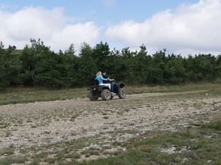 Young man and woman people riding without protective gear on a black Quad bike on a background of forest and blue sky with clouds on a Sunny summer day