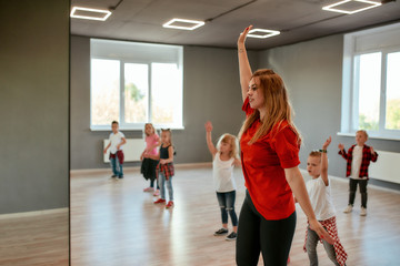 Naklejka na ściany i meble Step by step. Group of little boys and girls dancing while having choreography class in the dance studio. Female dance teacher and children