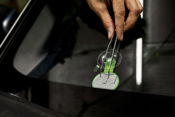 After a stone hit a windshield, a chipped glass formed. A man shows the place of impact on the windshield with tweezers and a mirror so that it can be seen better.