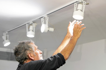Elderly caucasian electric man changes ceiling LED lamps, spotlight. The concept of repair and...